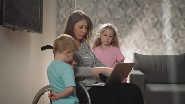 Mother shows kids pictures on laptop sitting in wheelchair