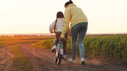 mother teaches child ride two-wheeled bicycle sunset. happy family. chidhood dream. girl with mom...