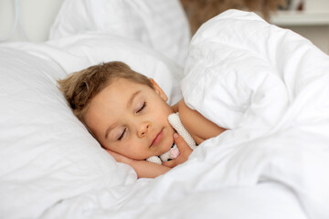 Fototapeta na wymiar Beautiful blond toddler child, boy, sleeping in bed with teddy bear toy