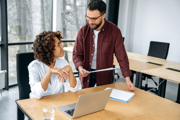 African american woman and caucasian man, company colleagues, work together on a project in a modern office, advise each other, share ideas and solutions, plan a product promotion strategy, smile