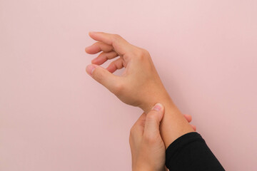 Close-up of woman's hand holding her painful wrist from Arthritis or Carpal Tunnel Syndrome (CST) isolated on pink background. Health care concept.