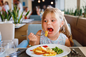 Adorable little girl having breakfast at resort restaurant. Happy preschool child eating healthy...