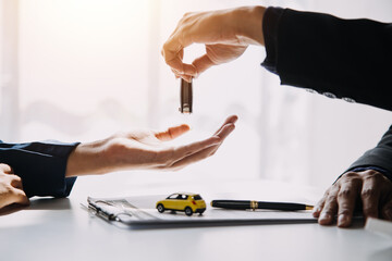 A car rental company employee is handing out the car keys to the renter after discussing the rental...