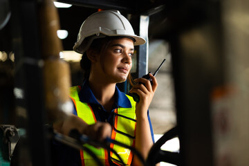 Indian woman worker driving a forklift and using a walkie-talkie at warehouse factory container. communication radio. Inventory and wholesale concept - obrazy, fototapety, plakaty
