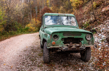Plakat An old shabby terrain car on a rural road. A battered cark is parked on an old dirt road in a high-altitude forested area