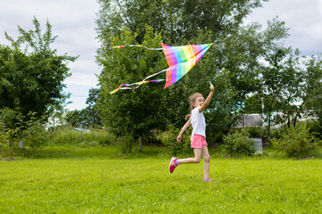 cheerful happy little girl is flying a rainbow kite. kids summer fun. summer vacation for kids. childhood holiday concept