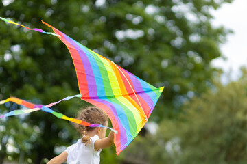 cheerful happy little girl is flying a rainbow kite. kids summer fun. summer vacation for kids. childhood holiday concept. soft focus