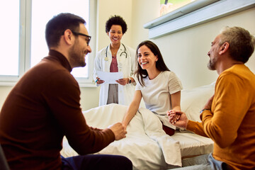 A smiling adult female patient held hands with her family during the visit in presence of the female doctor.