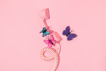 Spring creative layout with pink retro phone handset with colorful butterflies  on pastel pink background. 80s or 90s retro fashion aesthetic telephone concept. Minimal romantic cosmetic idea.