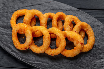 Delicious golden battered, breaded and deep fried crispy onion rings on black wooden table
