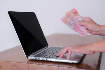 Close up: A woman's hand on keyboard laptop, other hand holding money.