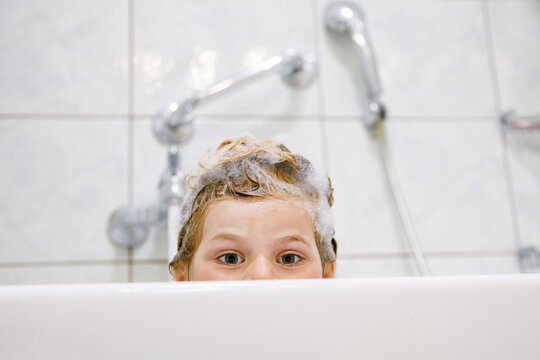Cute child with shampoo foam and bubbles on hair taking bath. Portrait of happy smiling preschool girl health care and hygiene concept. Washes hair by herself.