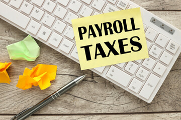 payroll taxes . text on yellow sticky note and work desk with white keyboard