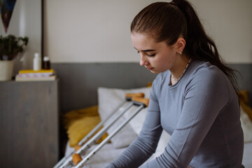 Unhappy teenage girl with broken leg sitting on a bed.