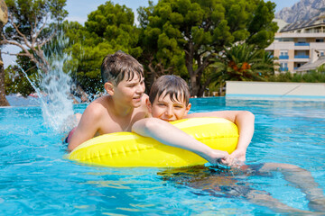 Two kids boys having fun on inflatable rubber rings in outdoor pool. Summer holiday. Summertime...