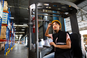 Asian female warehouse worker drive forklift in warehouse. Warehouse staff worker by goods shelf working in large warehouse factory