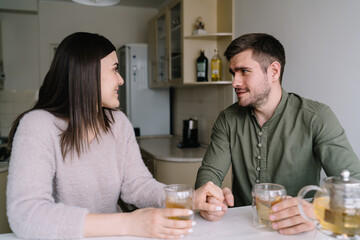 Happy couple sitting at table and drinking tea in kitchen