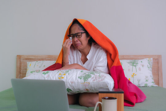 A woman sitting on bed watching film on her laptop, crying.