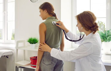 Teen girl on checkup appointment with young woman doctor examining her in clinic using...
