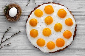 Homemade German Fried Egg Cake Spiegeleierkuchen with apricot and milk pudding on a light background with tulips. Traditional Easter Dessert. Festive Easter food.