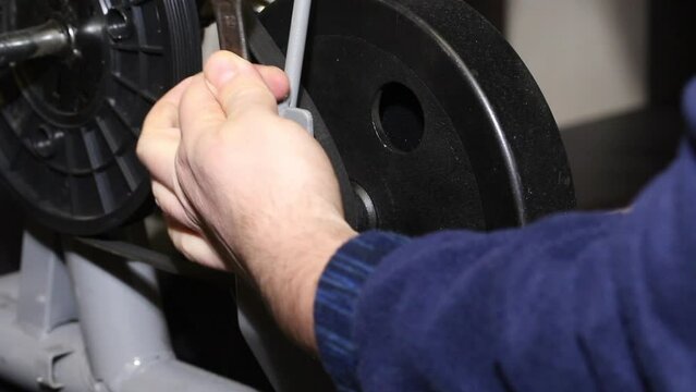 A man loosens the flywheel nuts in an exercise bike. With a wrench. Loosen the drive belt tension. Close-up.
