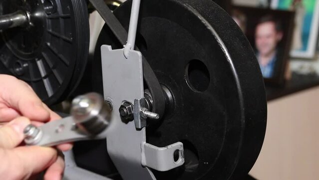 A man examines a pressure roller for a belt drive. Loosen the flywheel to install the pressure roller on the exercise bike. Close-up.