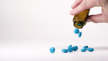 Blue pills falling out from a traditional pharmacy bottle. Treatment and prevention of diseases. Male hand holding a brown bottle. Assortment of medicinal pharmaceutical products with white background