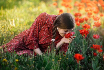 A girl sniffs red poppies in a meadow