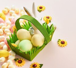 Happy Easter. Easter eggs and rabbit in green basket on pink background with white and yellow roses. Spring Happy Easter holiday card.  Easter background with copy space. Top view.