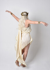 Full length portrait of beautiful blonde woman wearing a fantasy goddess toga costume with  magical crown.
Standing pose, facing backwards away from camera.  isolated on white studio background.