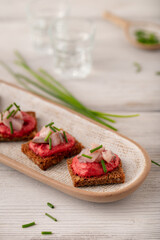 Bruschetta with herring and beetroot puree on a plate and shots with vodka decorated with scallions on a light wooden table background. Closeup. Selective focus