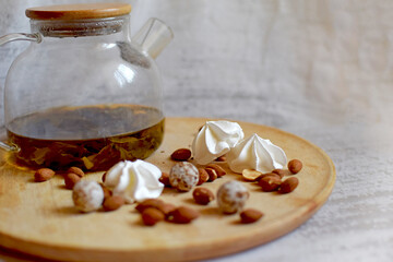 A teapot with tea, sweets, almonds and meringue grains  (marshmallows) lie on a wooden tray.