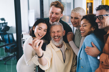 Laughing multiethnic coworkers with smartphone smiling and taking selfie together