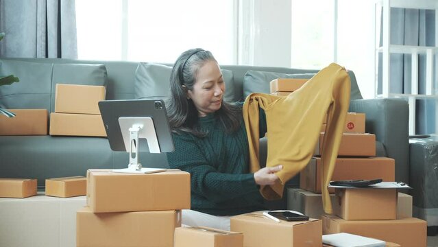 Successful asia people woman entrepreneur with parcel boxes clothing online store checking email order in tablet and laptop at sofa home office SMEs small company.