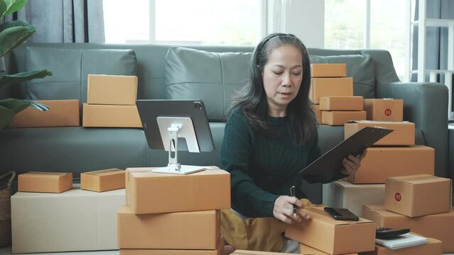 Successful asia people woman entrepreneur with parcel boxes clothing online store checking email order in tablet and laptop at sofa home office SMEs small company.