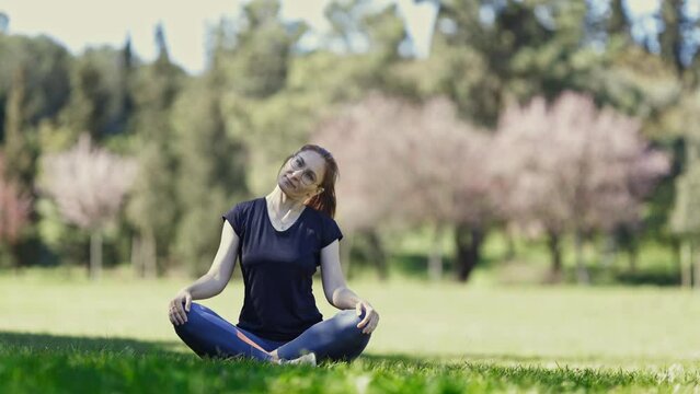 Smiling adult woman in glasses sits in the lotus position and warming up her neck