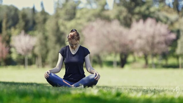 An adult woman in glasses sits in the lotus position and warming up her neck