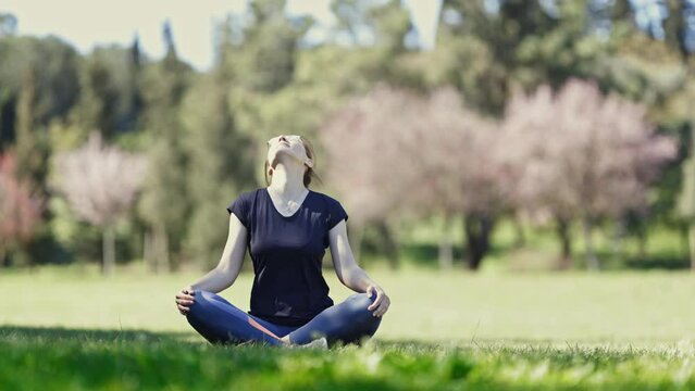 Doing yoga on nature - a woman in glasses sits in the lotus position and warming up her neck