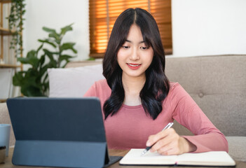 Young female listening to lecture, engaged in internet educational course, remote education , working online. Head shot focused woman taking notes watching webinar, studying online at home, .