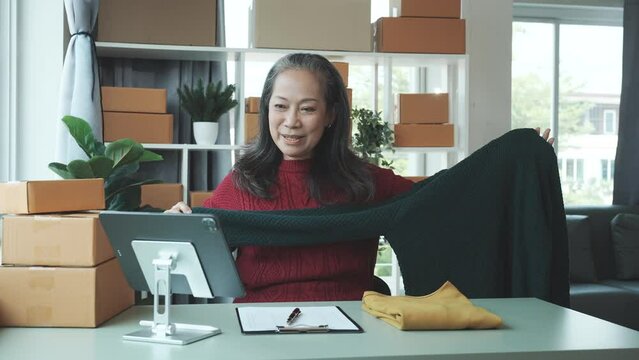 Successful asia people woman entrepreneur with parcel boxes clothing online store checking email order in tablet and laptop at sofa home office SMEs small company.