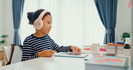 Asian toddler girl with sweater wear headphone sit front of desk with notepad use magic pen focus on writing do homework, finger counting number math online learning course from laptop at home.