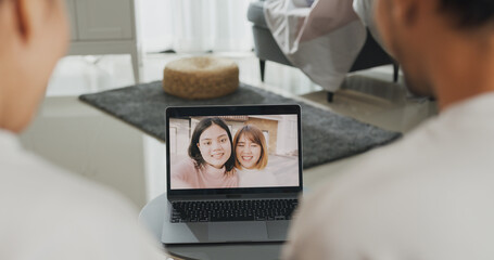 Happy young Asian couple sit on couch smiling looking at laptop screen talk video call with friends...