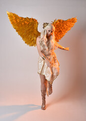 Full length portrait of beautiful blonde woman wearing a fantasy goddess toga costume with feathered angel wings. Jumping pose like flying, isolated on white studio background.