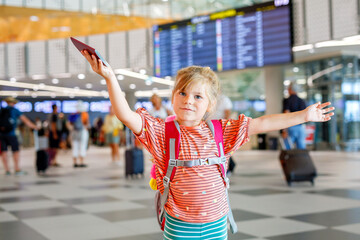 Little preschool girl at airport terminal. Happy child going on vacations by airplane. Smiling kid with passport and bag.