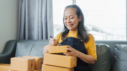 Successful asia people woman entrepreneur with parcel boxes checking email order in tablet and laptop at sofa home office SMEs small company.