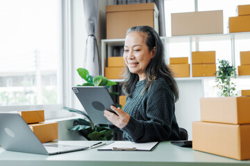 Successful asia people woman entrepreneur with parcel boxes clothing online store checking email order in tablet and laptop at sofa home office SMEs small company.