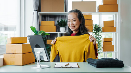 Successful asia people woman entrepreneur with parcel boxes clothing online store checking email order in tablet and laptop at sofa home office SMEs small company.