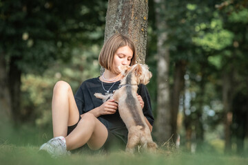 Portrait of a young beautiful fair-haired girl with a thoroughbred Yorkshire terrier in a summer park.