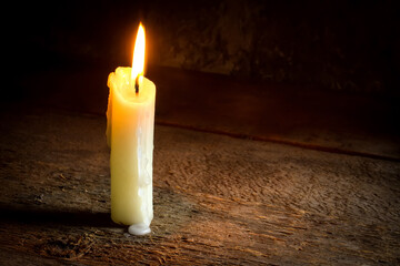 A lit candle against a background of rough wood.