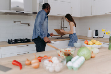 A happy young couple is busy in the kitchen. A black man and a young girl are washing dishes and cooking